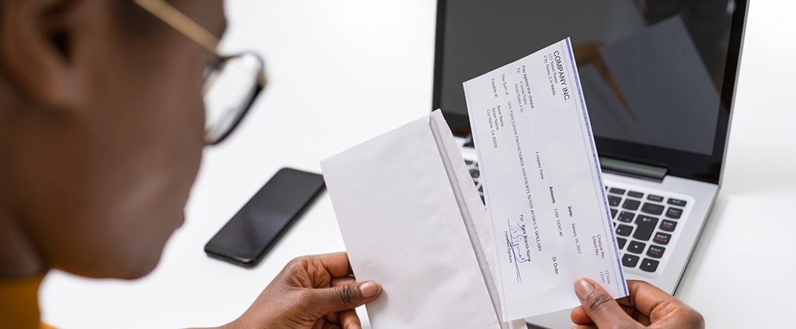 Woman removing a check from an envelope with a laptop and smartphone on her desk