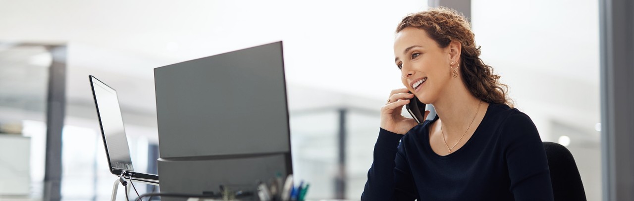 A woman talks on the phone while looking over her computer
