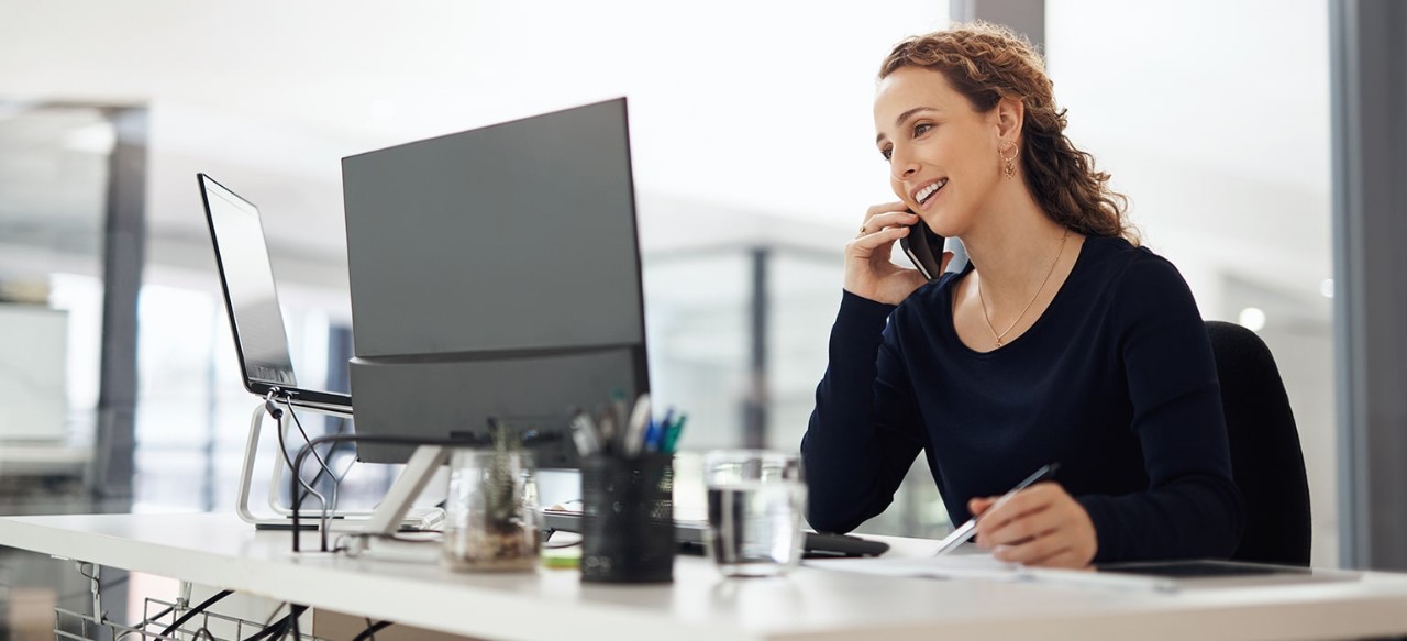 A woman talks on the phone while looking over her computer