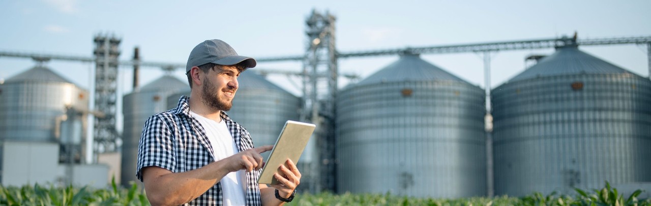 Farmer using tablet in front of grain elevators