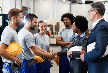 Employees with hard hats meeting with bankers in warehouse facility