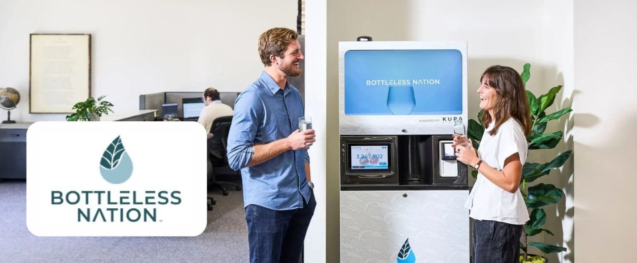 Two young workers in an office talking and smiling around a modern water dispenser, adjacent to superimposed Bottleless Nation logo