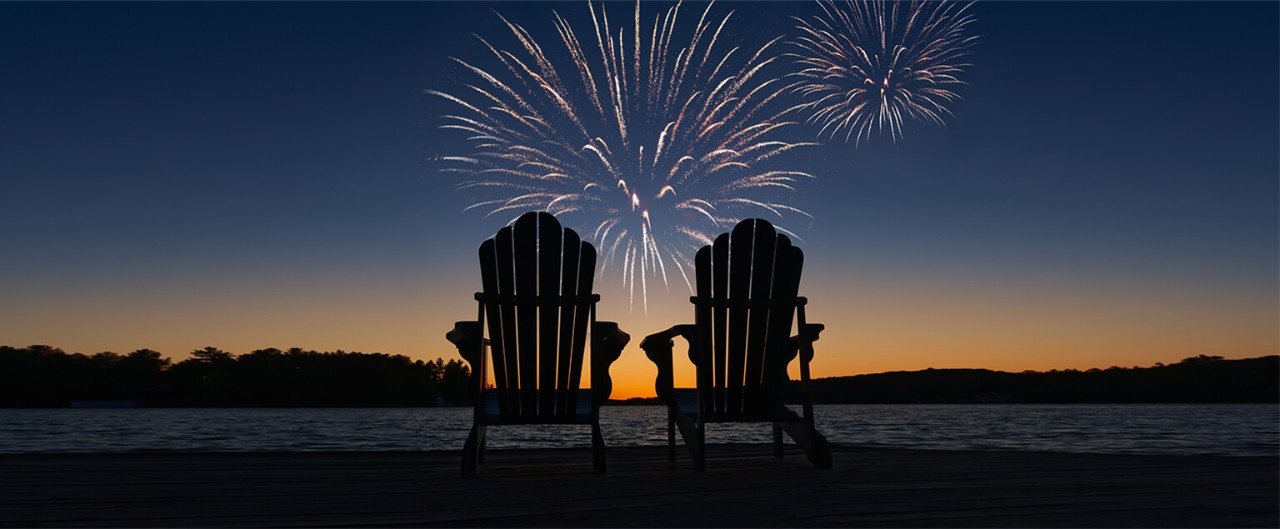 Two empty Adirondack chairs in front of a twilight fireworks display