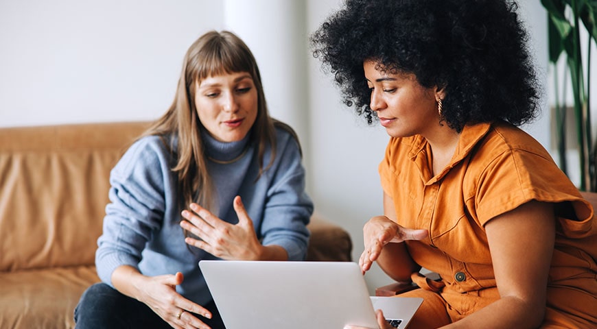 Two women conversing while looking at a laptop