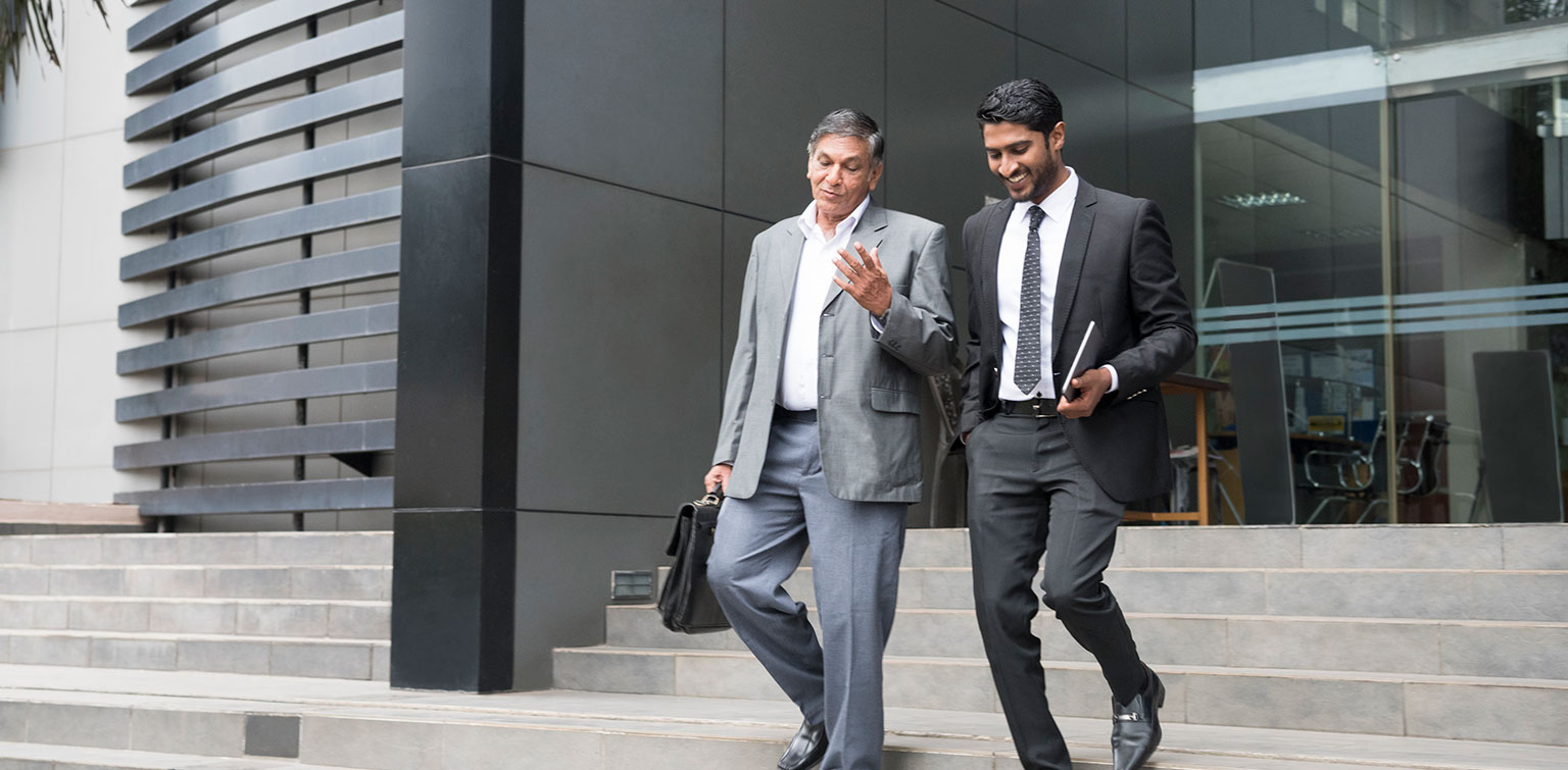 Older businessman talking with younger colleague as they leave the office