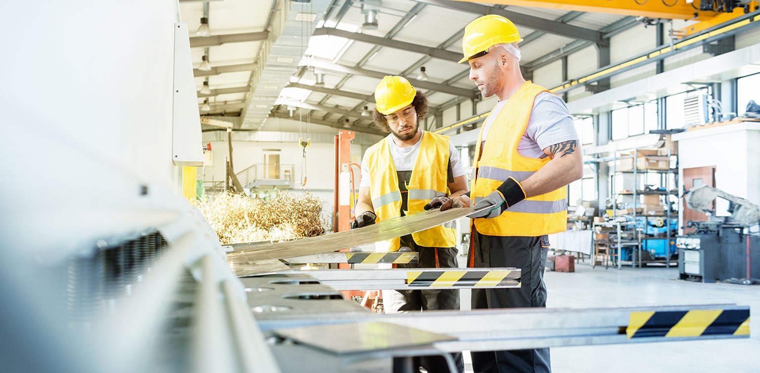 Two men in hard hats and high-visibility vests working in a manufacturing facility