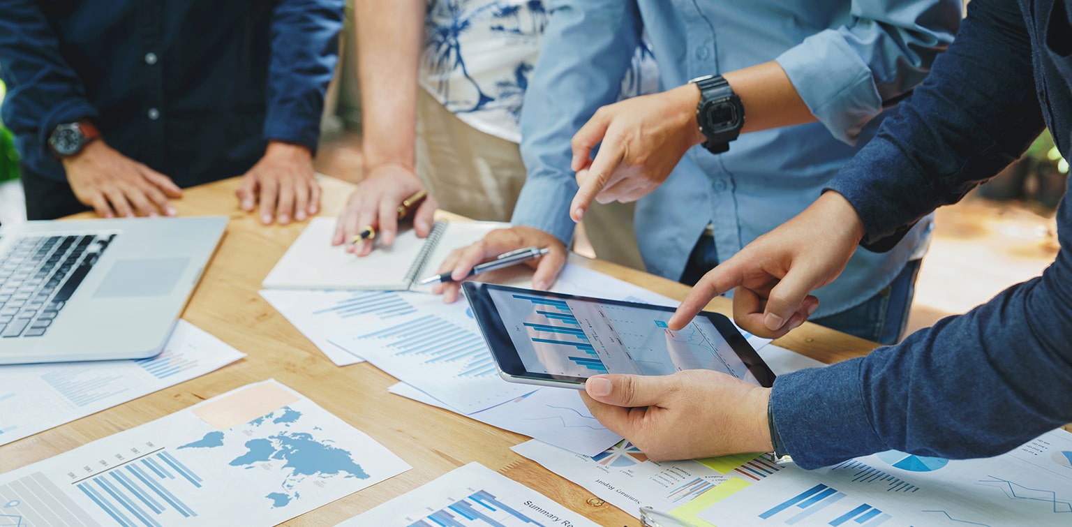 A group of people around a table with charts and graphs and a tablet