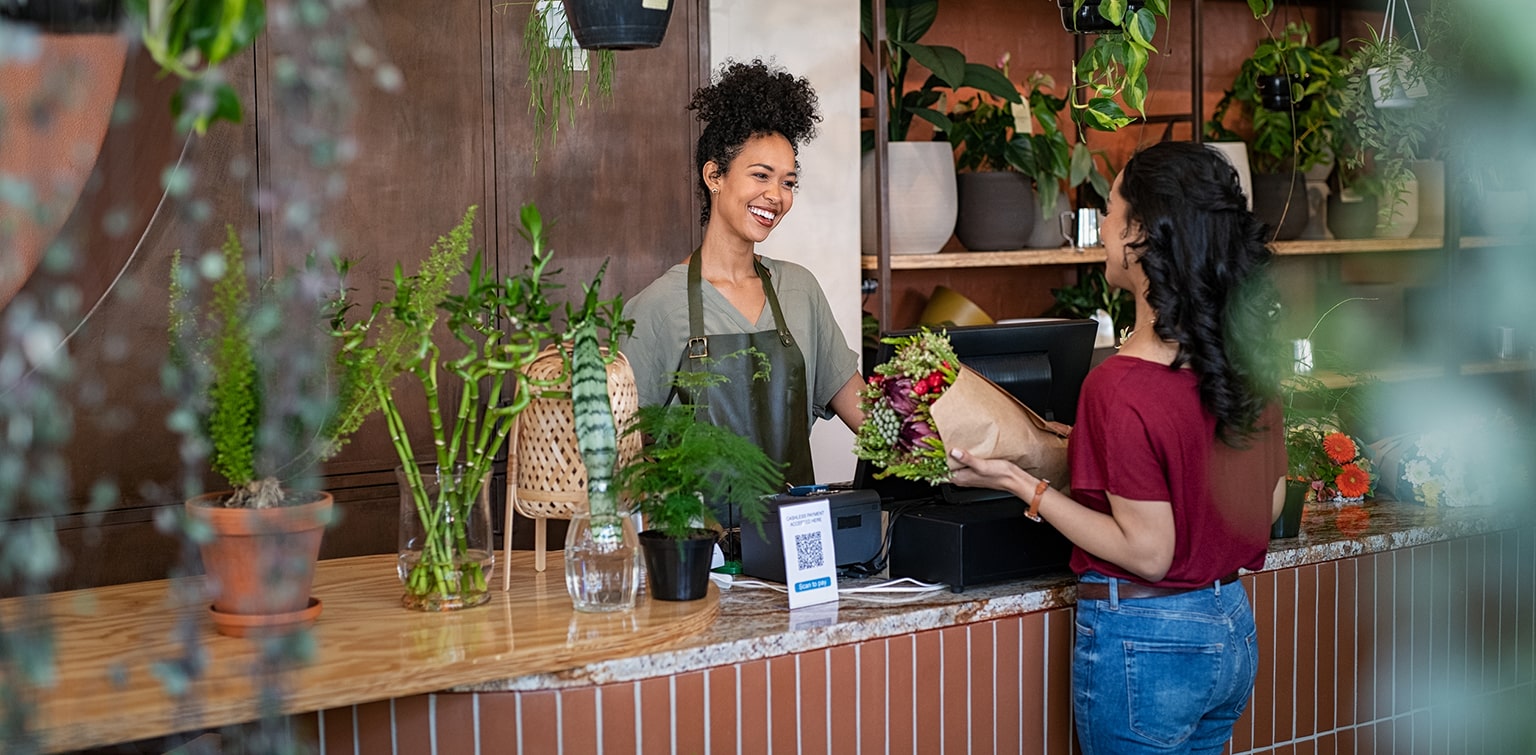 Happy female florist selling bouquet to female customer