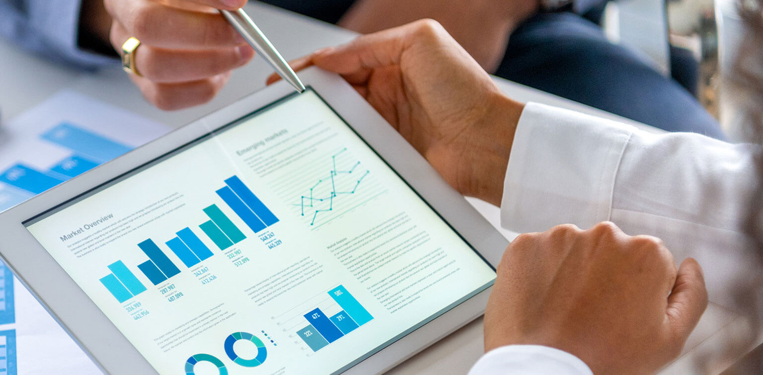 Close-up of people's hands as they review financial data on a tablet and paper documents