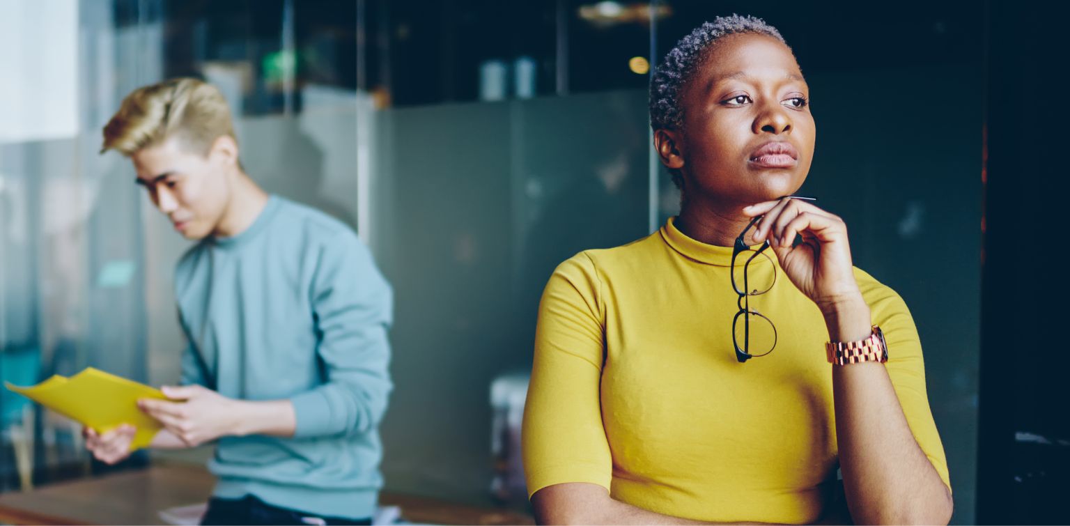 Businesswoman with close-cropped gray hair holds glasses under her chin and gazes into distance with concern