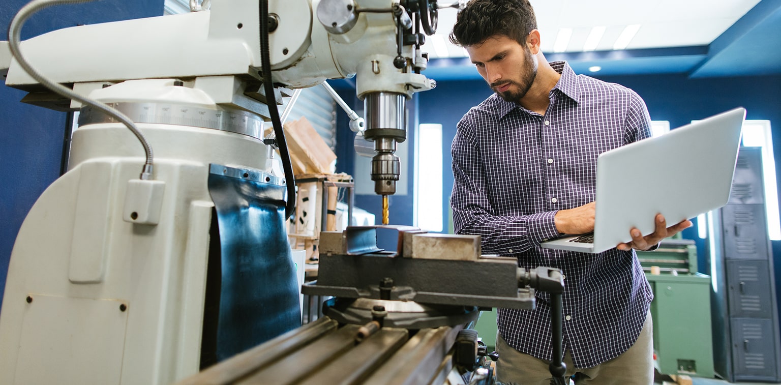 A man with a laptop looks over machinery