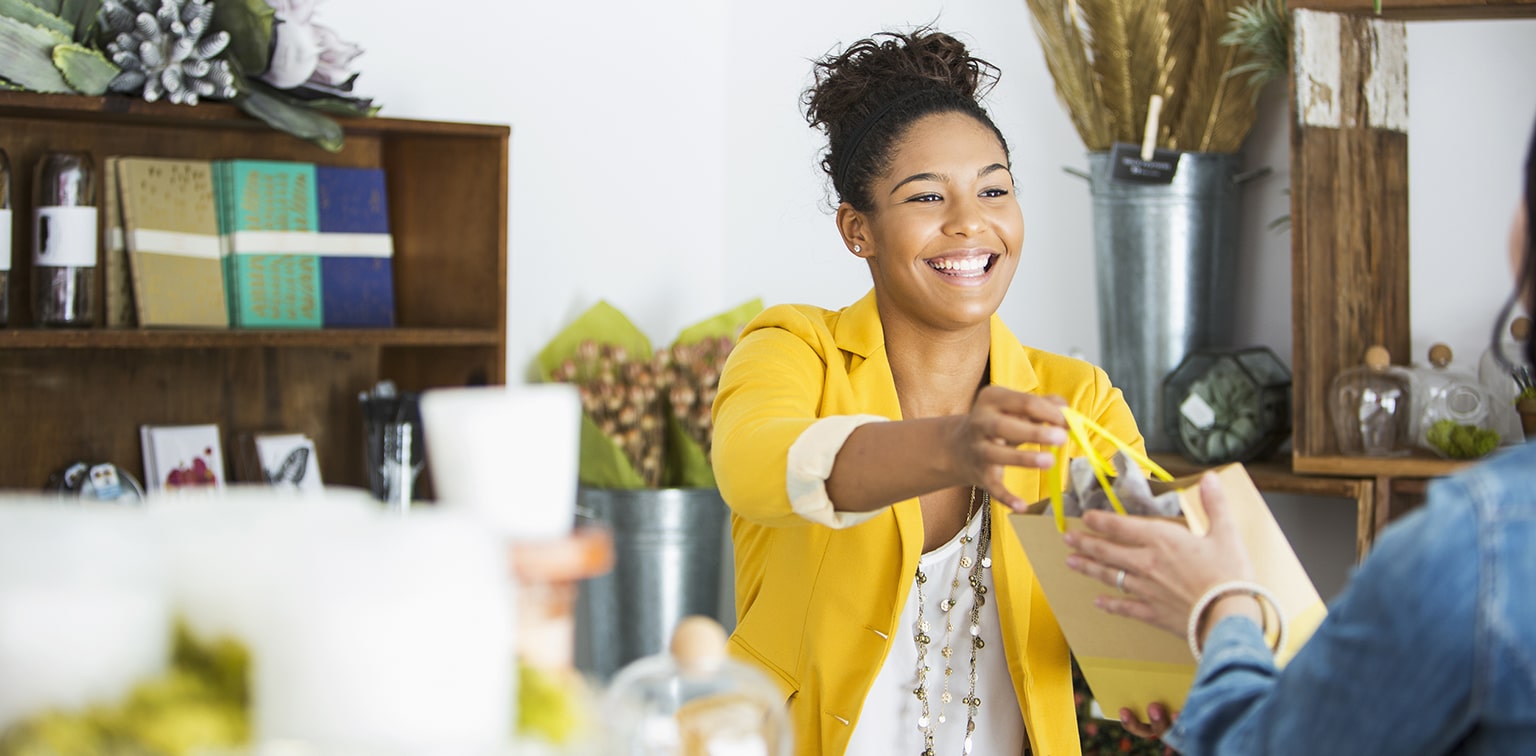 Friendly African-American boutique owner handing customer a gift bag