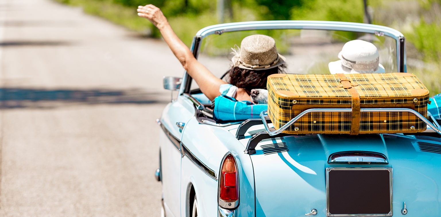 Women in vintage convertible with suitcase on trunk rack