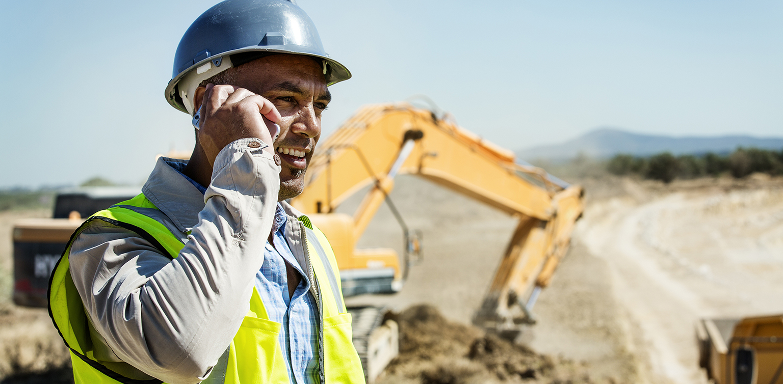 Hispanic construction foreman on phone with bulldozer in background