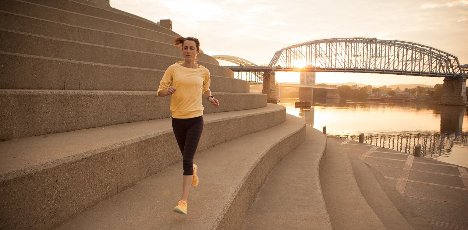 Woman running on steps of Serpentine Wall with Ohio River and bridge in background