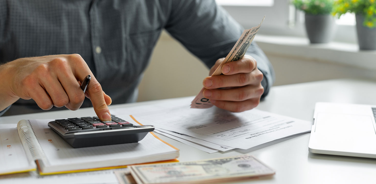 Man holding cash and using calculator to pay bills