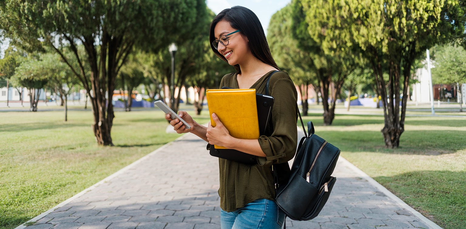 Female Hispanic college student wearing backpack, holding leather portfolio and a smartphone