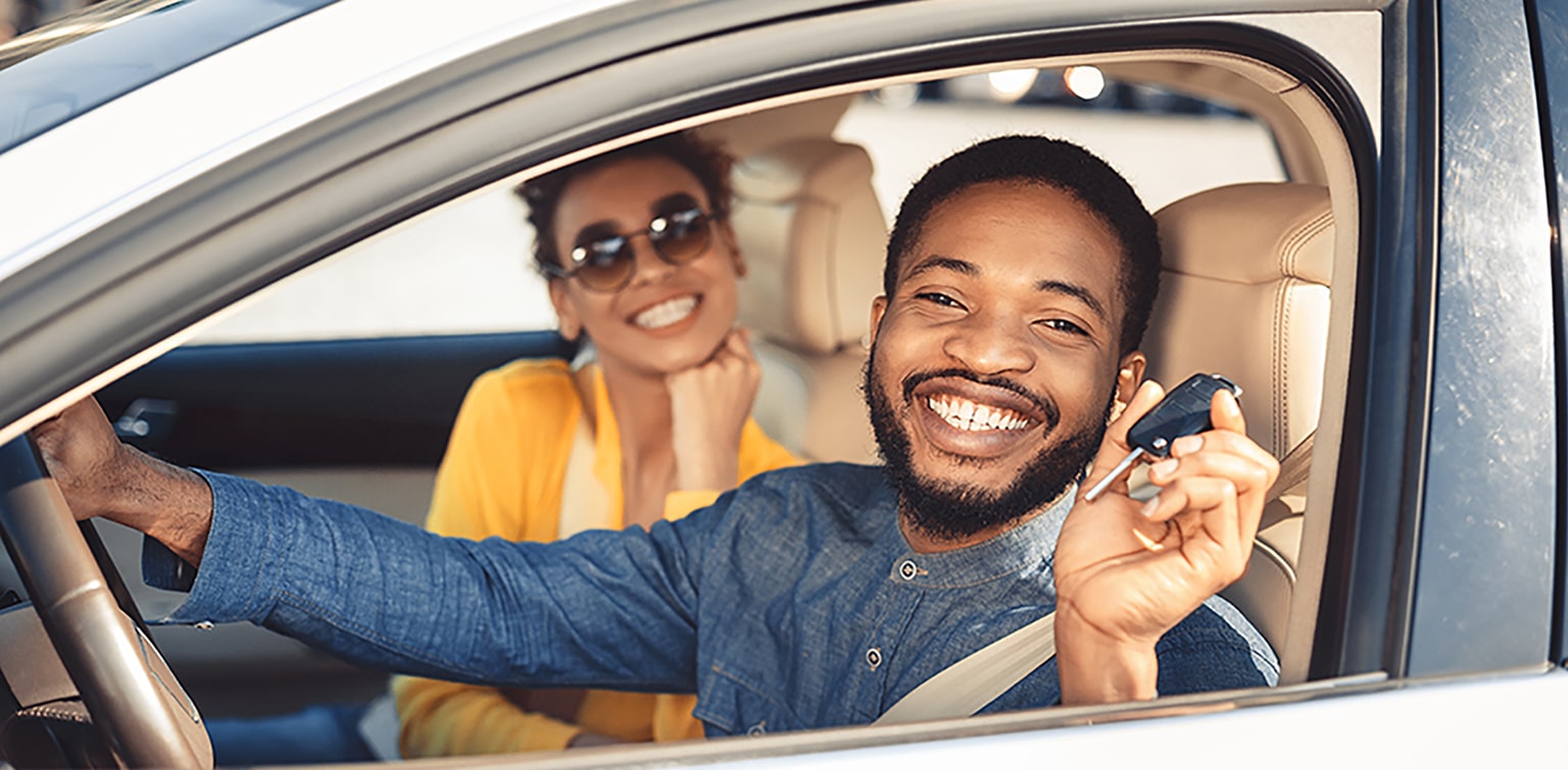 Happy African-American couple sitting in new car holding keys