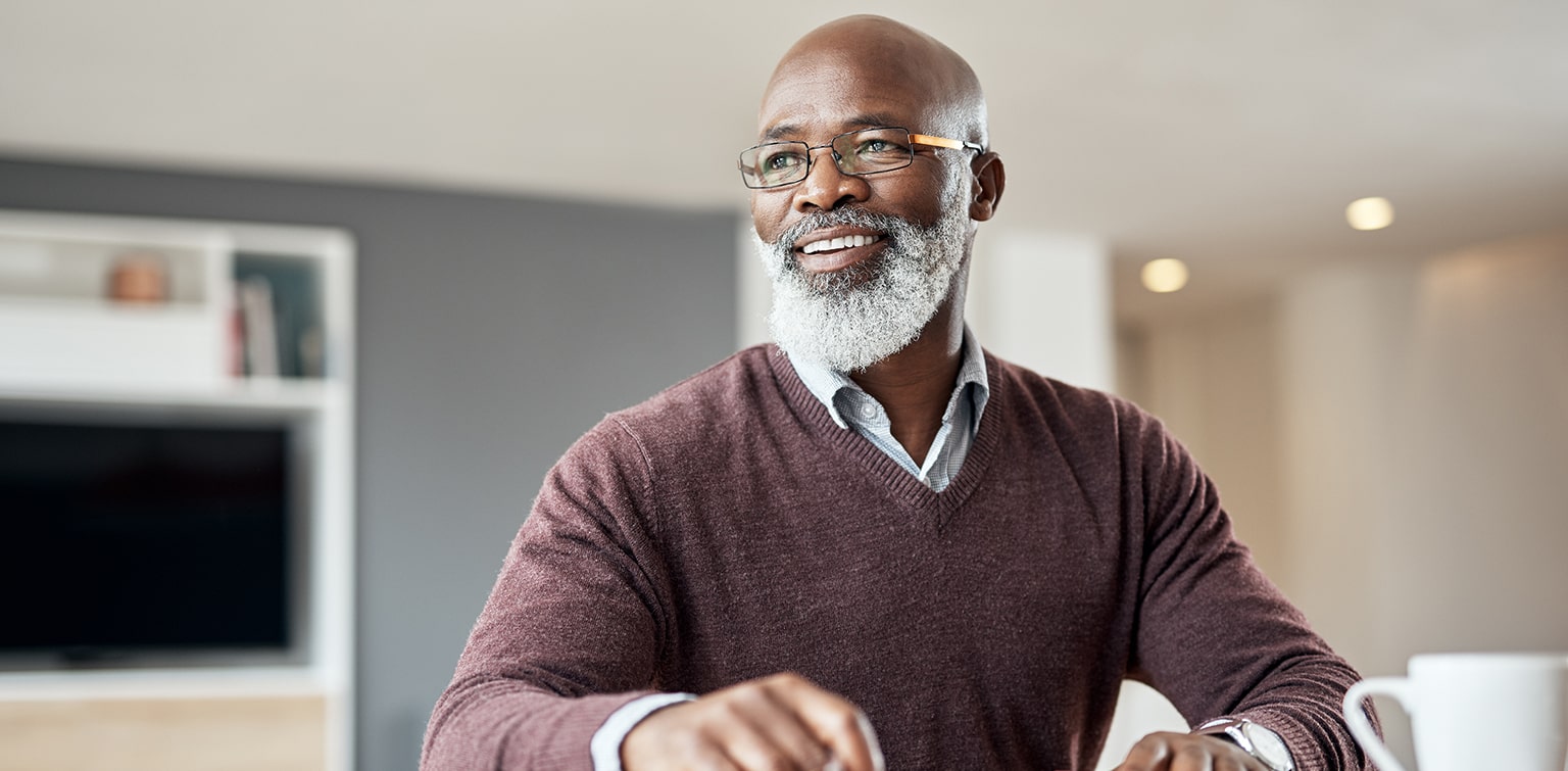 Smiling senior African-American man sitting alone in his living room and thinking how to use strategic asset allocation