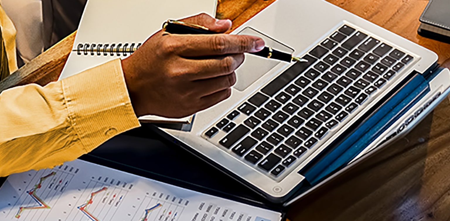 Man at desk with financial papers pointing pen at laptop