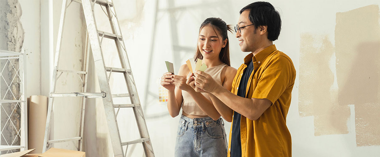 Smiling Asian couple comparing paint swatches in a room being renovated