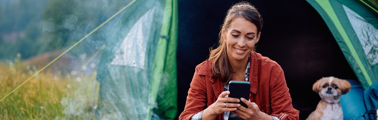 Young woman in a tent with a small dog, using smartphone