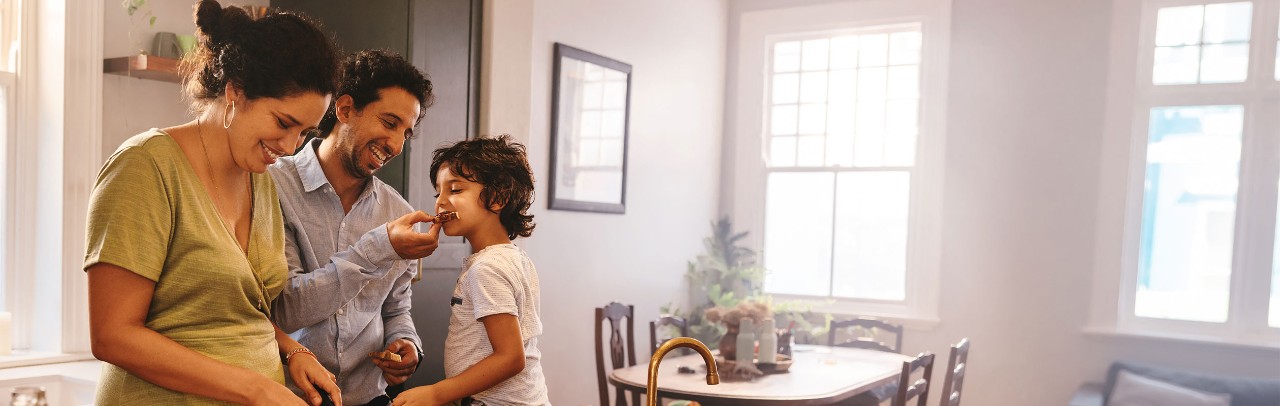 Smiling parents preparing breakfast while young son sits on kitchen counter