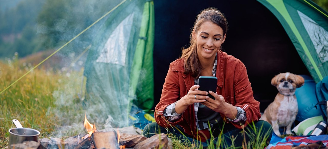 Young woman in a tent with a small dog, using smartphone