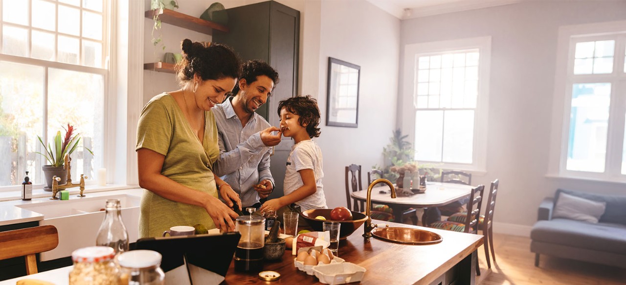 Smiling parents preparing breakfast while young son sits on kitchen counter