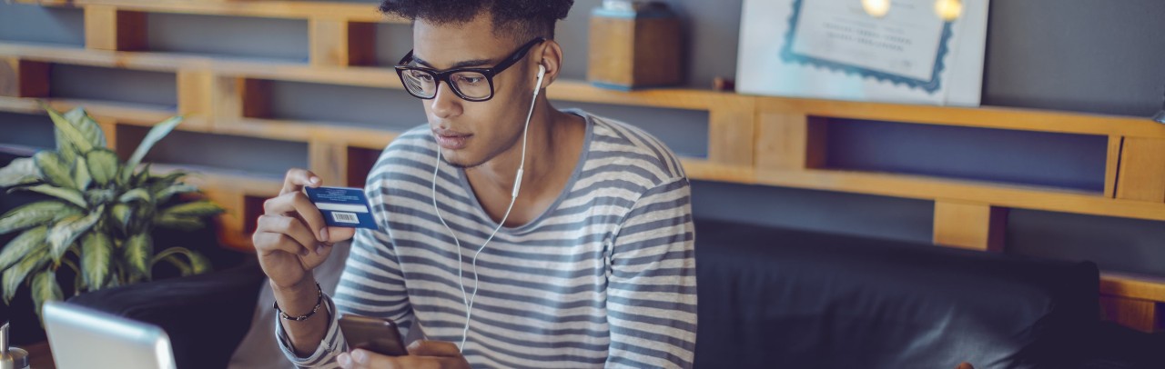 Young African-American man holding bank card and smartphone