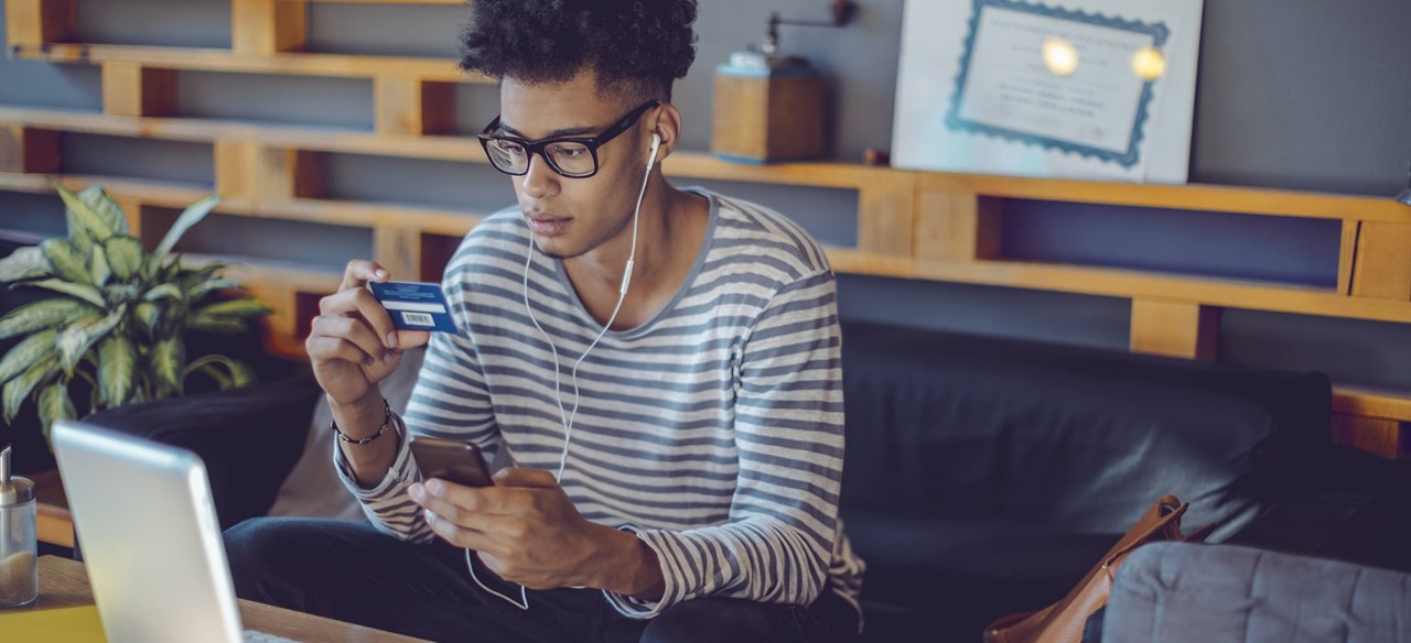Young African-American man holding bank card and smartphone