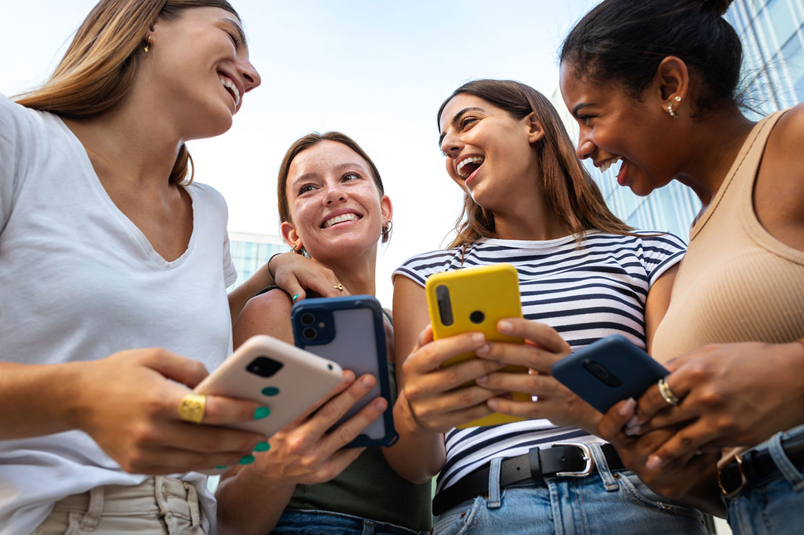 Four smiling young women using smartphones