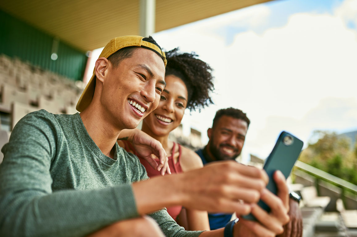 Three diverse friends sitting on stadium bleachers looking at a smartphone