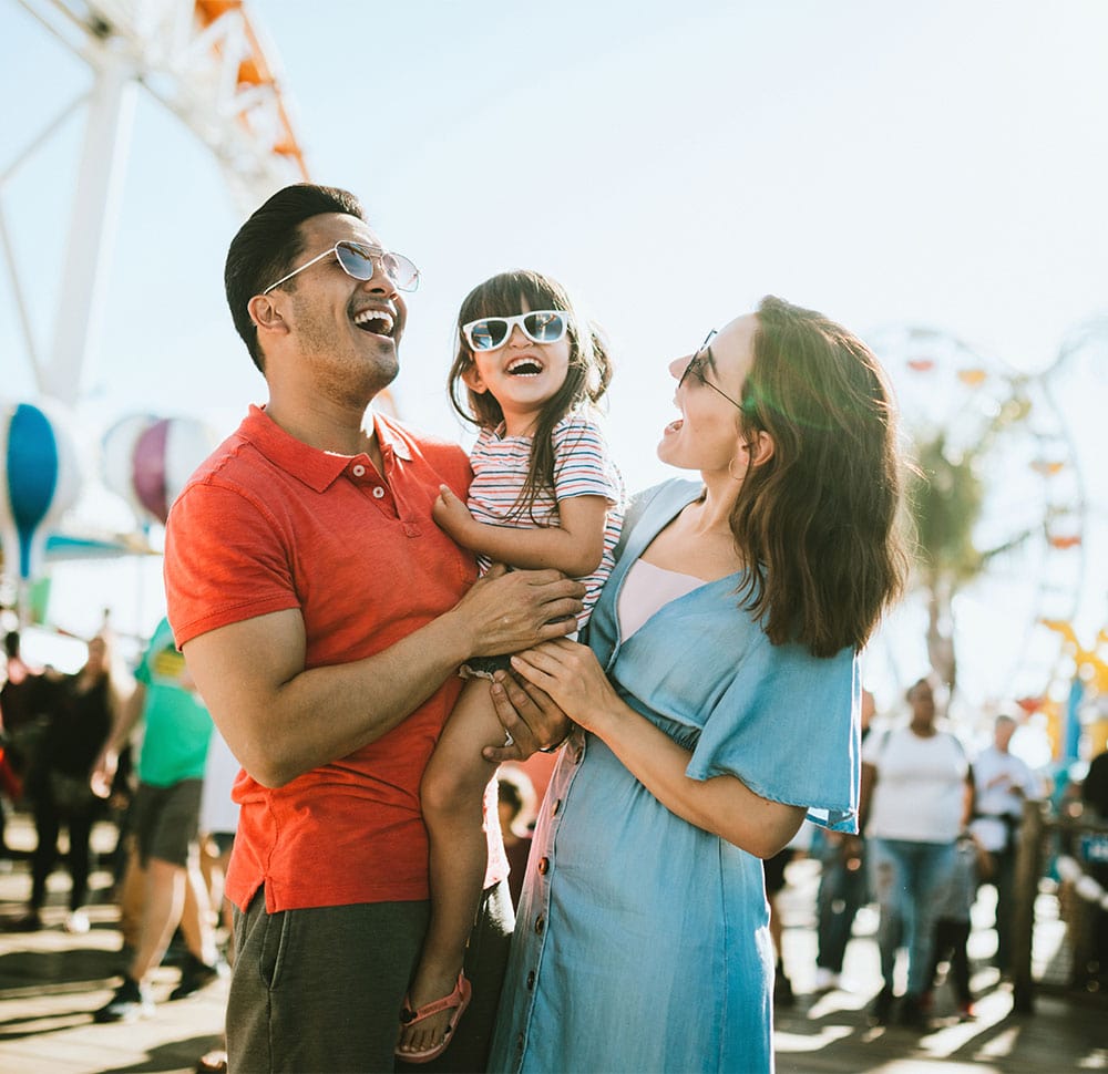 Smiling multi-ethnic parents holding young daughter at amusement park