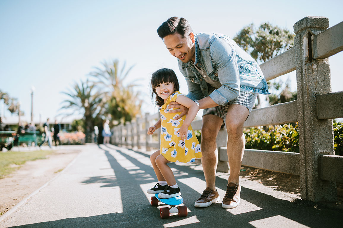 Father helping his young daughter ride a skateboard