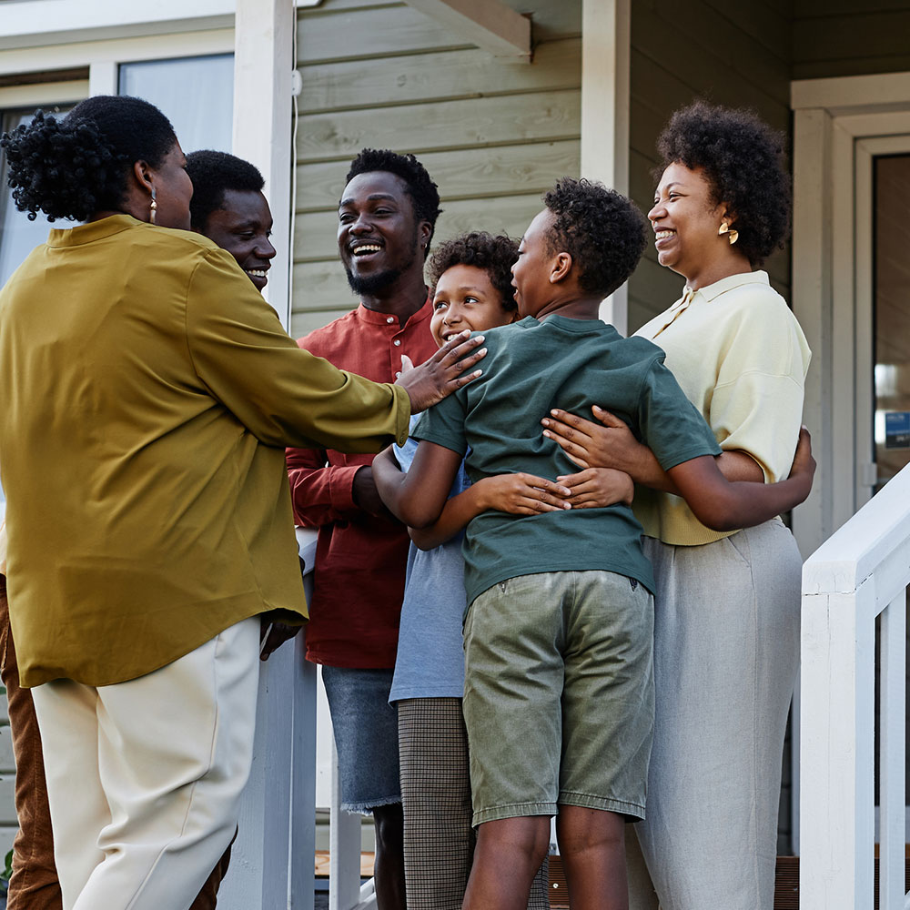 Multigenerational African-American family embracing in front of house