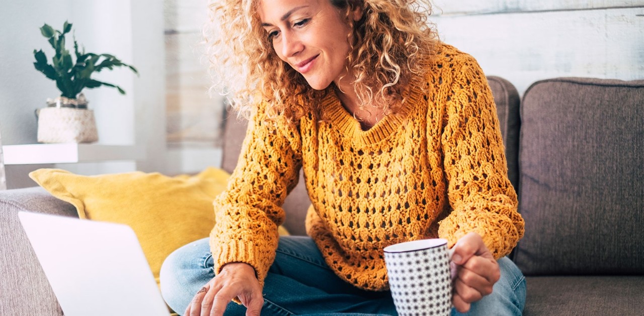 Caucasian woman holding a coffee mug and working on a laptop