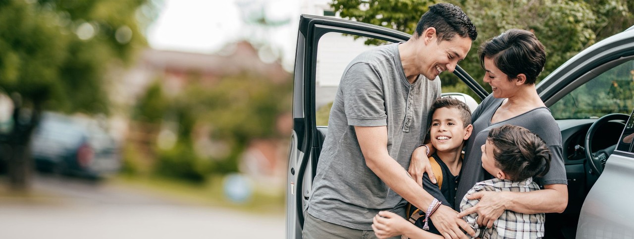Hispanic parents hugging two young sons near a car