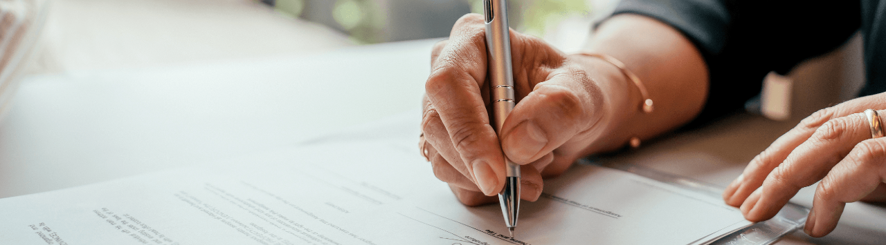 Person signing financial documents with a pen during a professional meeting