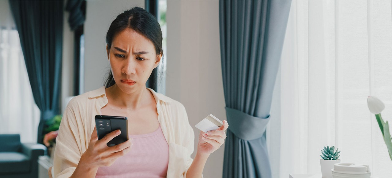 Asian-American woman with concerned expression looking at smartphone and holding credit card