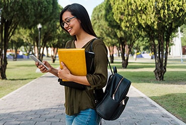 Female Hispanic college student wearing backpack, holding leather portfolio and a smartphone