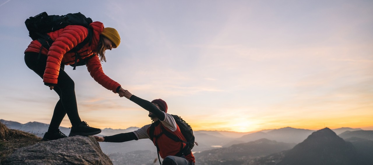 Woman offering man an outstretched hand as he climbs a mountain