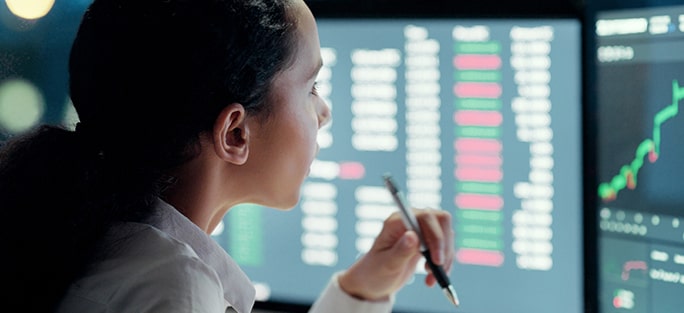 Female analyst reviewing financial data on multiple monitors