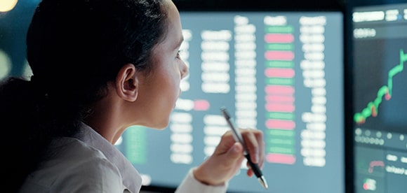 Female analyst reviewing financial data on multiple monitors