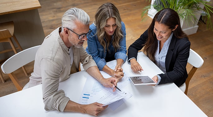 Couple reviewing documents and data on a tablet with their financial advisor